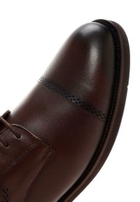 Zapato de vestir de cuero marrón con un acabado pulido, punta redondeada y perforaciones decorativas a lo largo del costado. Presenta cordones y un pequeño tacón.