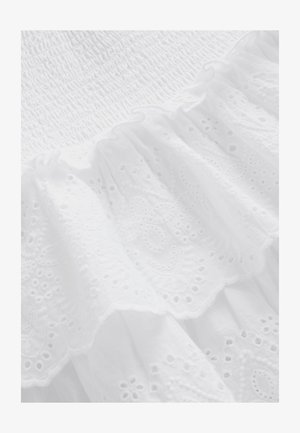 Witte stof met gerimpelde structuur bovenaan, gelaagd met gerimpelde kant met bloemmotieven en kleine openingen langs de zoom.