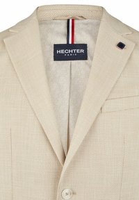 Beige strukturiertes Blazerjacke mit Reverskragen, Einknopfverschluss und Logoschild, gepaart mit einem gemusterten Futter und dezenten Akzentfarben.