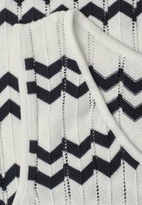 Tissu tricoté blanc avec des rayures chevron noires et des détails de points ouverts verticaux, plié pour montrer la texture et le motif en gros plan.