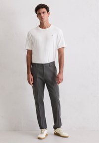 Weißes T-Shirt mit kurzen Ärmeln, graue, maßgeschneiderte Hose und cremefarbene Sneaker. Einfaches Design, glatte Textur und dezentes Branding auf dem T-Shirt.