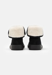 Botas de tobillo de ante negro con un cuello de piel sintética blanca y una suela de goma negra texturizada, diseñadas con una parte superior doblada.