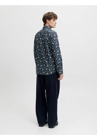Camicia floreale blu navy con maniche lunghe, colletto button-down e piccolo motivo a fiori bianchi, abbinata a pantaloni neri larghi e scarpe nere.