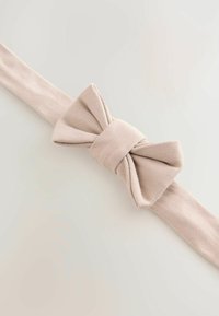 Beige kangasvyö, jossa suuri rusetti keskellä; sileä pinta ja suorakulmainen muoto. Pehmeä, neutraali väri, sopii monenlaisiin asuihin.