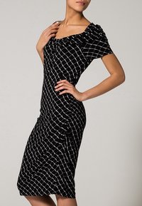 Svart klänning med vitt rutmönster, korta ärmar och rynkad halsringning. Figurformad med rynkade detaljer och knälång slits.