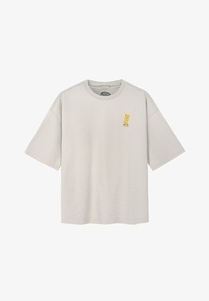 Jasnobeżowy, oversize T-shirt z krótkimi rękawami, z małą żółtą grafiką i tekstem na lewej stronie klatki piersiowej.