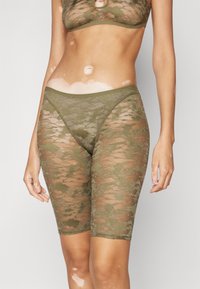 Calções de renda verde-oliva com um padrão floral, comprimento até a metade da coxa, apresentando uma cintura lisa e seções transparentes para adicionar textura.