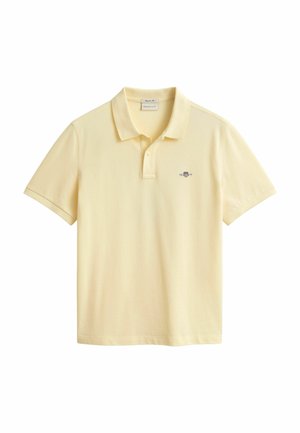 Polo à manches courtes jaune clair avec col et patte à deux boutons, arborant un petit logo brodé sur le côté gauche de la poitrine.