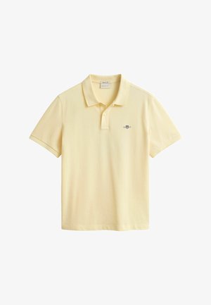 Polo à manches courtes jaune clair avec col et patte à deux boutons, arborant un petit logo brodé sur le côté gauche de la poitrine.