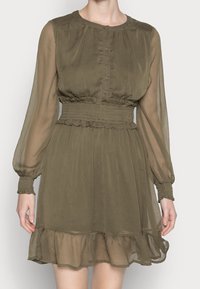 Vestido verde oliva hecho de una tela transparente, con escote redondo, botones frontales, mangas largas con puños acampanados y un dobladillo con volantes en capas.