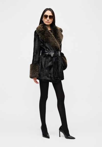 Μαύρο γουνάκι με φαρδιά καφέ γουνώδη γιακά και ταιριαστά μανσέτες, ζώνη στη μέση. Φορεμένο με μαύρο κολάν και ψηλοτάκουνες γόβες.