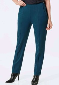 Tegengroene broek gemaakt van een gladde stof, met zijzakken en een recht gesneden ontwerp. Draag met zwarte puntige hakken.