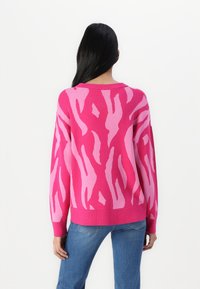 Rosa tröja med kontrasterande ljusrosa abstrakt tigerstripemönster, ribbat nacke och ärmslut, lös passform, matchad med blå jeans.