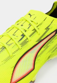 Lyse gul fodboldstøvle med sorte zigzag-mønstre, tekstureret overdel og en rød- fremhævet logo. Snørebåndene er neon gule.
