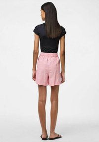 Šviesiai rožiniai ir balti dryžuoti šortai su elastine juosta, demonstruojami ant asmens, kuris vilki juodą trumpą rankovę ir šlepetes.