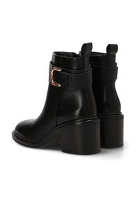 Botas de cuero negras hasta el tobillo con punta redonda, tacón grueso y un acento de hebilla dorada en una correa. Textura suave y diseño elegante.