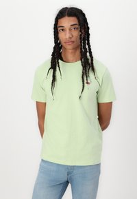 Lysegrøn bomulds t-shirt med korte ærmer og rund hals, med et lille rødt Levi's-logo på brystet, båret med lyseblå jeans.