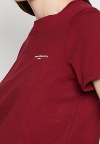 Rød bomulds t-shirt med rund hals, korte ærmer og et lille hvidt logo på brystet. Blød og glat tekstur.