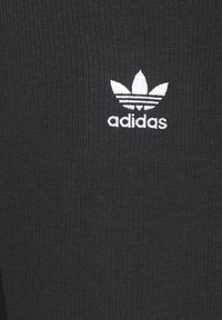 Černá žebrovaná tkanina s bílým logem "adidas" a akcentem ve formě tří pruhů. Materiál je elastický a přiléhavý, vhodný pro sportovní oblečení.