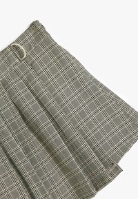 Falda a cuadros en blanco y negro, con un ojal para cinturón y una hebilla plateada, fabricada con un tejido texturizado entrelazado y diseño de plisados.