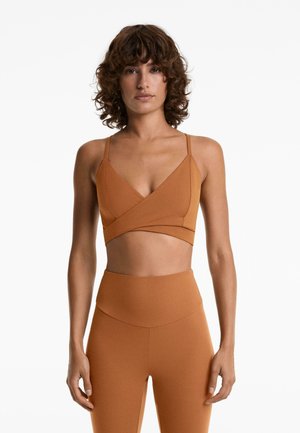 Bralet de antrenament maro cu decolteu adânc în V, design încrucișat în față și curele subțiri ajustabile, complementar cu colanți cu talie înaltă.