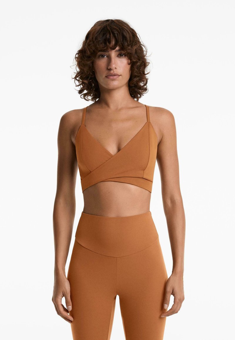Bruine sport-bralette met een diepe V-hals, kruislings ontwerp aan de voorkant en dunne verstelbare banden, gecombineerd met hoge taille leggings.
