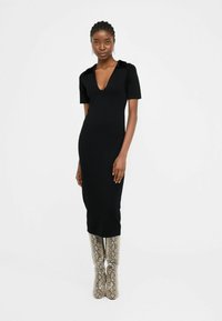 Abito midi in maglia nera con maniche corte e scollatura a V profonda, caratterizzato da un tessuto testurizzato e spalle decorate, abbinato a stivali al ginocchio con motivo.