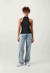 Must mustriba sleeveless topp, kõrge kaelusega, koos helesiniste laiade pükstega ja valgete tennisetega. Lisatud on selged raamistiku prillid.