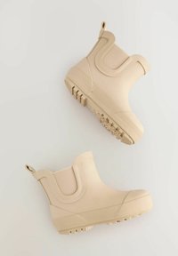 Beige vandtætte ankelstøvler med gummibyggeri, elastiske sidepaneler, tekstureret sål og en trækstrop for nem påtagning.