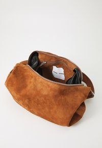 Borsa in suede marrone con chiusura a zip, dotata di un interno in pelle nera. La borsa presenta una superficie morbida e texture e una forma informale.