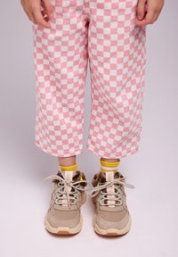 Sneaker beige con dettagli in pelliccia e lacci a pois, abbinate a calzini gialli. I pantaloni a quadri rosa e bianchi sono cropped e dal fitting morbido.