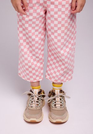 Sneaker beige con dettagli in pelliccia e lacci a pois, abbinate a calzini gialli. I pantaloni a quadri rosa e bianchi sono cropped e dal fitting morbido.