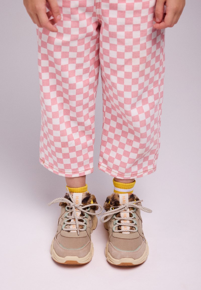 Sneaker beige con dettagli in pelliccia e lacci a pois, abbinate a calzini gialli. I pantaloni a quadri rosa e bianchi sono cropped e dal fitting morbido.