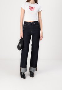 Camiseta corta blanca con el texto rojo "HACER LLORAR A LOS CHICOS", combinada con jeans de pierna ancha de mezclilla oscura con puños azul claro y botas de tobillo negras.