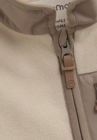 Beige fleece jacket with a high collar, featuring a zip closure and tan accents. Includes a leather logo patch and textured fabric.
