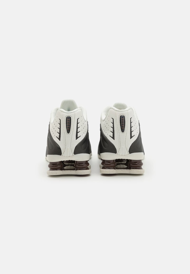 Schwarz-weiße Sportschuhe mit einem strukturierten Obermaterial, ausgestattet mit einer gepolsterten Ferse und einer braunen Gummisohle. Reflektierende Akzente an den Seiten.
