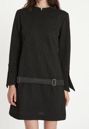 Czarna sukienka z długim rękawem z pionowymi srebrnymi prążkami, wykrojem z wycięciami, wydłużonymi mankietami i błyszczącym paskiem z dwoma klamrami w talii.