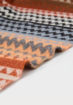 Multicolored blanket with a zigzag pattern featuring shades of rust, cream, black, and brown. Made of soft, textured fabric.