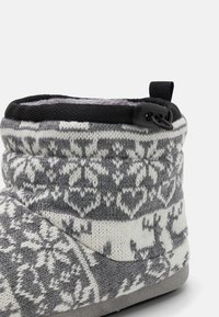 Gray and white knitted slipper, featuring a Fair Isle pattern with deer and snowflakes, soft lining, and a black pull tab for easy wearing.