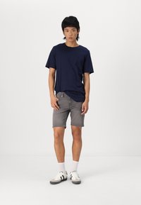 Marineblaues Baumwoll-T-Shirt, graue Denim-Shorts, weiße Socken und graue Sneaker mit schwarzen Akzenten. Schlichter, lässiger Schnitt mit entspannter Passform.