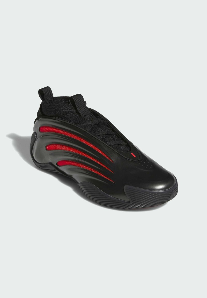 Chaussure de sport noire au design épuré, avec des accents rouges, une surface texturée et une semelle arrondie. Lacets élastiques et languette de traction inclus.