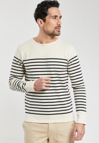Top a maniche lunghe color crema con righe orizzontali navy. Presenta un colletto a girocollo e maniche attillate, realizzato in un morbido tessuto testurizzato.