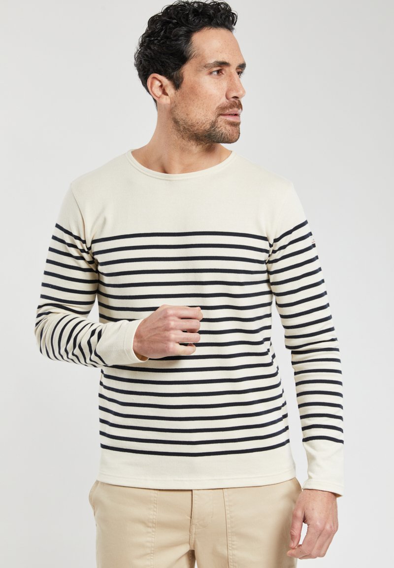 Top a maniche lunghe color crema con righe orizzontali navy. Presenta un colletto a girocollo e maniche attillate, realizzato in un morbido tessuto testurizzato.