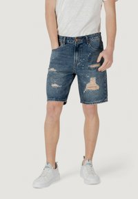 Shorts in denim blu scuro con effetto whiskering, strappi e leggeri orli sfilacciati. Abbinati a sneakers bianche e una t-shirt a righe.