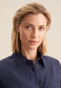 Chemise col marin de couleur bleu marine, en tissu texturé avec fermeture à boutons et un plastron court, offrant une coupe décontractée et des détails de couture subtils.