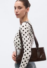 Ruskea nahkainen käsilaukku, jossa on jämäkkä muotoilu, kaksi hihnaa, hienovaraiset ompeludetaljit ja sileä pinta. Pallokuvioinen yläosa.