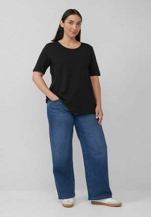 Schwarzes Kurzarm-T-Shirt, kombiniert mit locker sitzenden blauen Jeans und weißen Turnschuhen; gewagtes, lässiges Design mit rundem Ausschnitt.