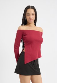 Rød, ribbet off-shoulder topp med lange ermer, har en splitt på siden, sammen med et svart minibånd. Glatt tekstur, tettsittende design.