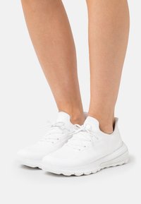 Zapatillas deportivas blancas con parte superior de punto, diseño de cordones, acentos texturizados y suela acolchada, que ofrecen un ajuste ligero y flexible.