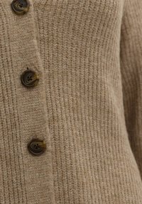 Beige gestrickte Strickjacke mit geripptem Muster, ausgestattet mit vier runden braunen Knöpfen auf der Vorderseite. Weiches Material mit einem warmen Aussehen.